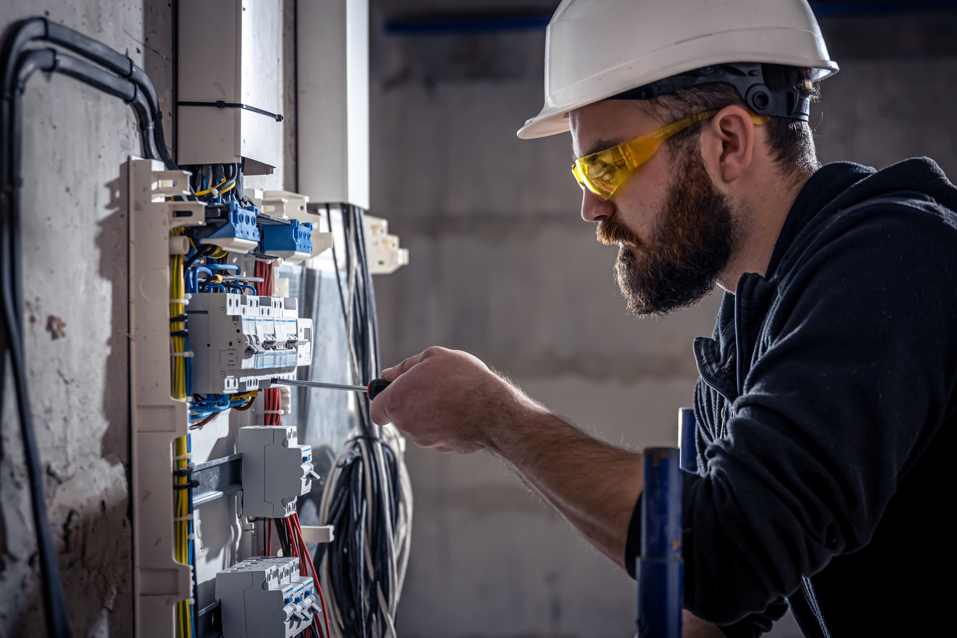 A male electrician works in a switchboard with an electrical connecting cable.